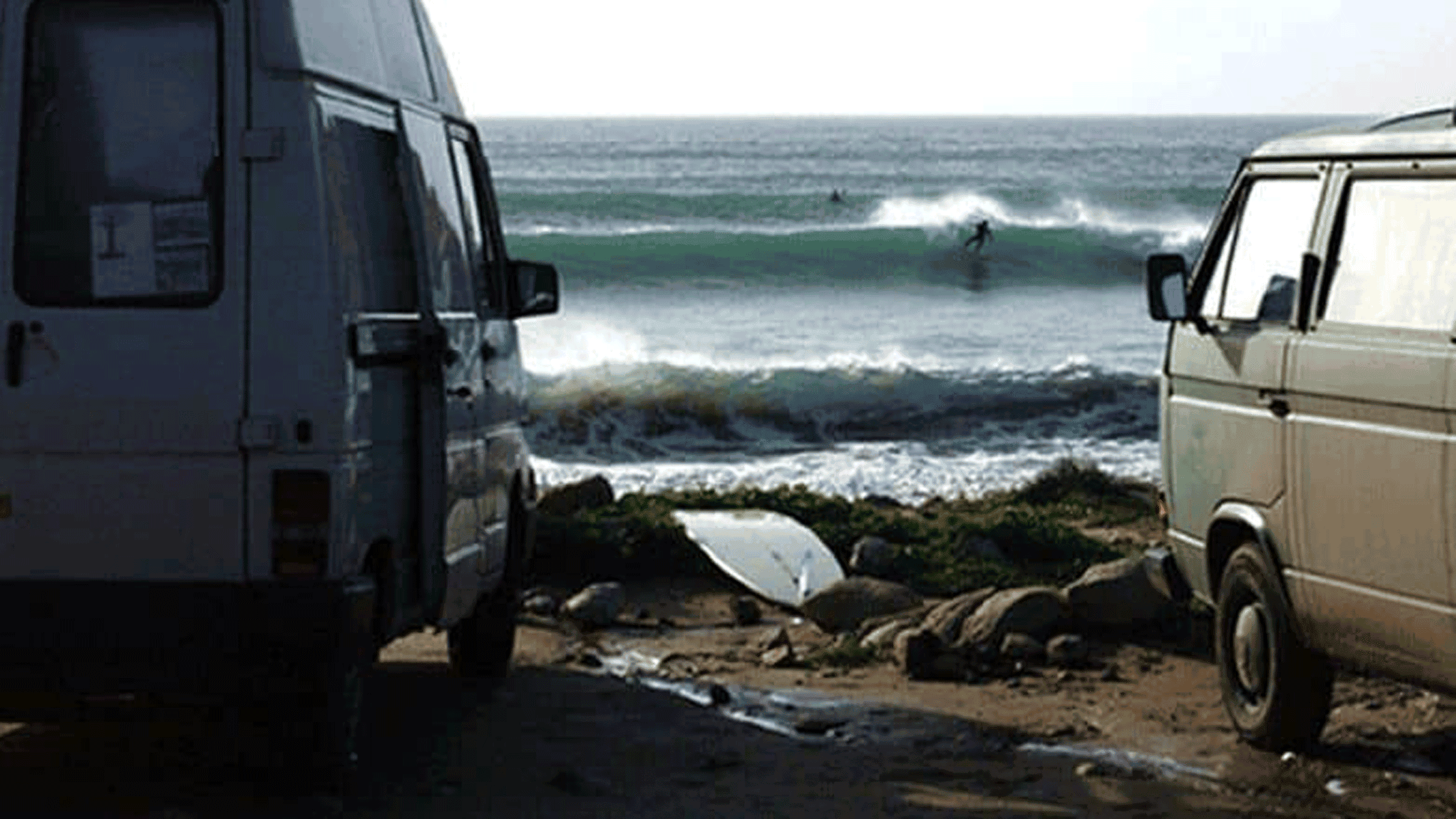 Two vans parked on sand with ocean waves crashing in the background.