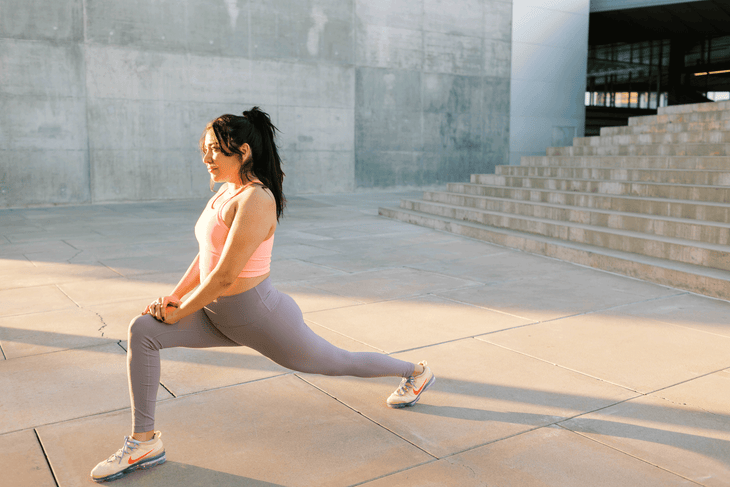 Woman in yoga leggings and sports bra practicing hip flexor stretches on concrete in downtown Phoenix.