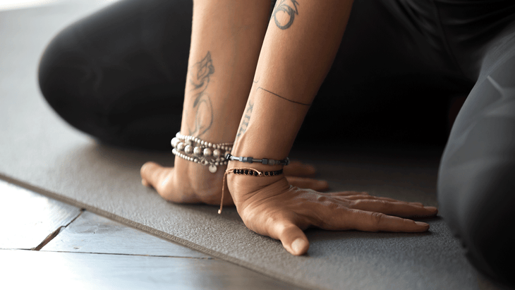 Yoga student sitting on a mat learning how to strengthen wrists and stretch them while wearing several different bracelets.