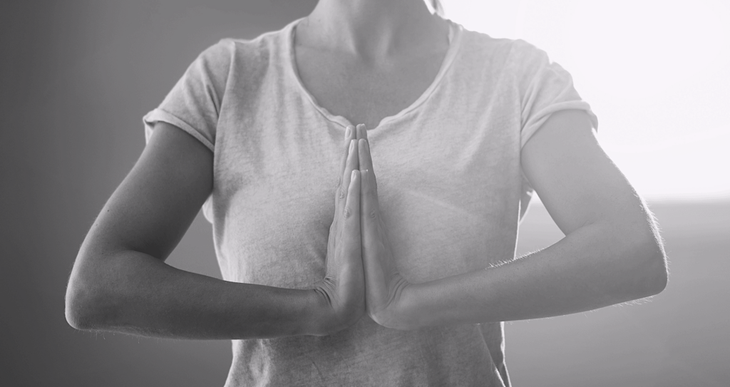 A black and white photo of a woman in a t shirt with prayer hands at her chest as she practices how to strengthen wrists.
