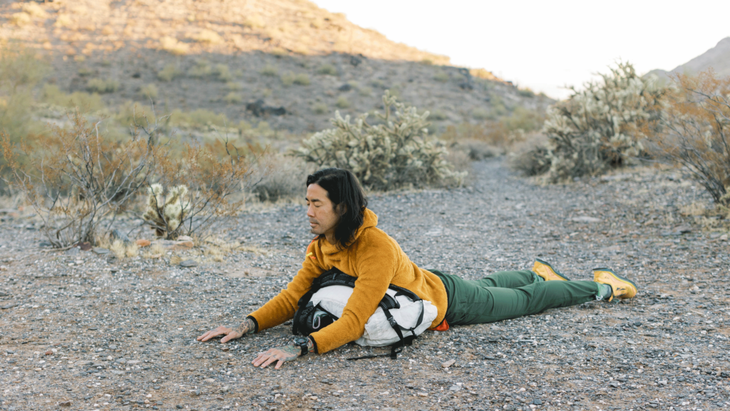 Backpacker practicing supported Sphinx Pose with a backpack beneath his chest.