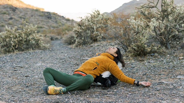 backpacking enthusiast doing yoga while laying on their backpack in the desert