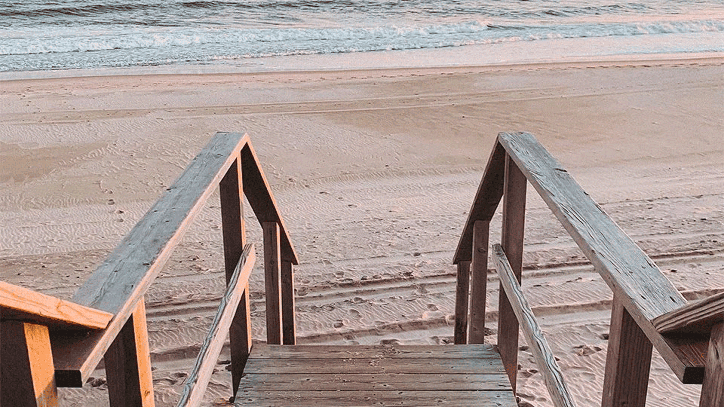 A wooden staircase leading to sand and ocean waves.