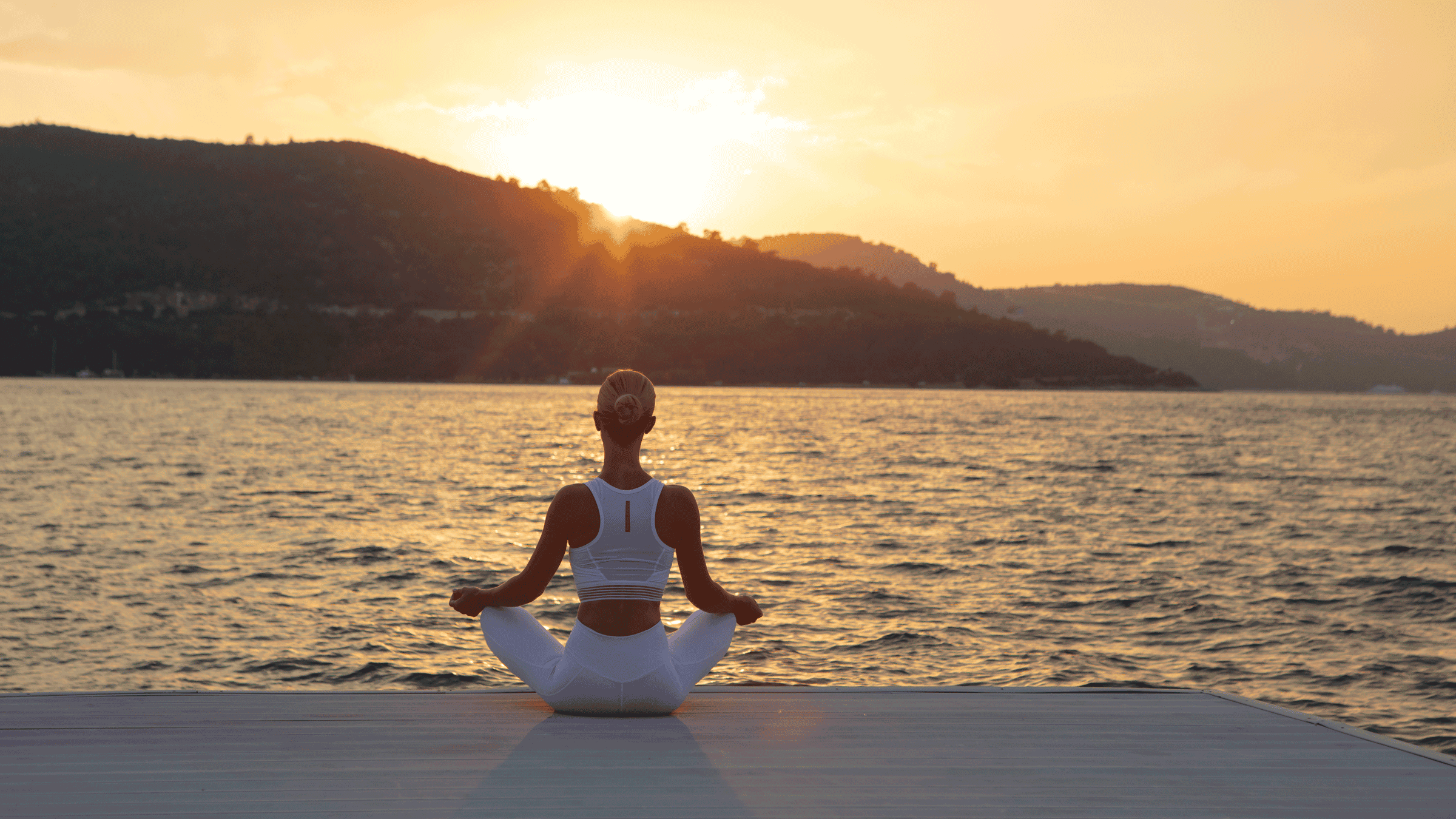 Woman sitting and meditating by the sea at sunset