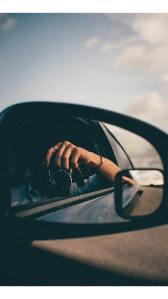 A selfie of a woman looking into the rearview mirror of a car while contemplating Mercury retrograde with its focus on looking backward
