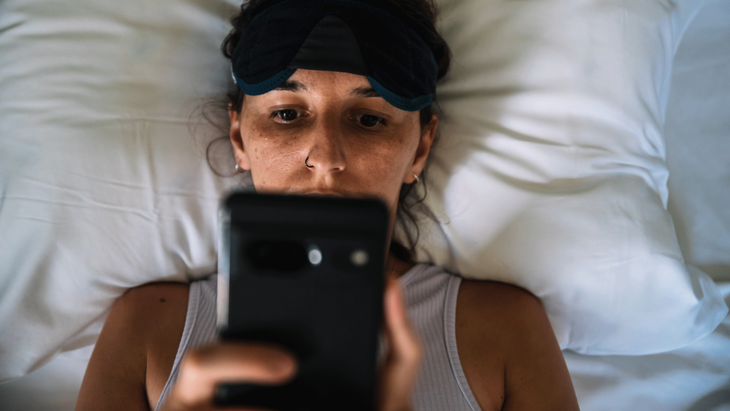 Woman lying in bed with her phone searching for a yoga nidra YouTube video