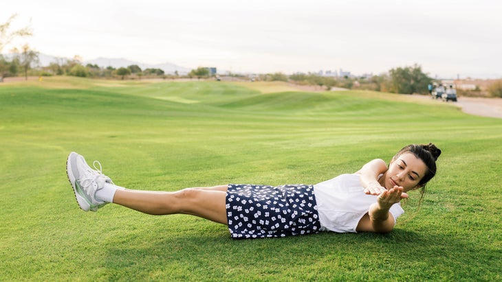 A woman performs yoga poses on a golf course doing a v-sit pose.