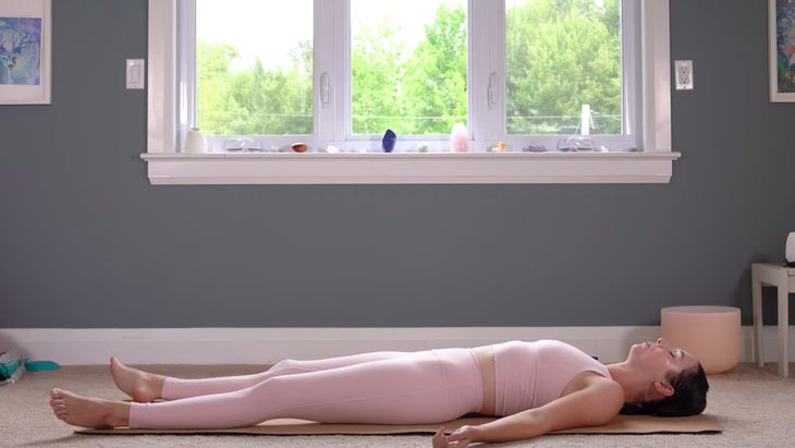 Woman lying on her yoga mat in Savasana while meditating