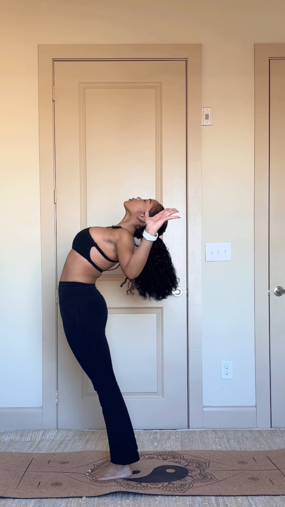 Woman standing on a yoga mat arching her back and taking her arms in a cactus shape