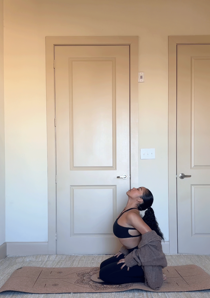 Woman kneeling on a yoga mat with her toes tucked under practicing arching her back in a 5-minute morning stretch known as Cow Pose