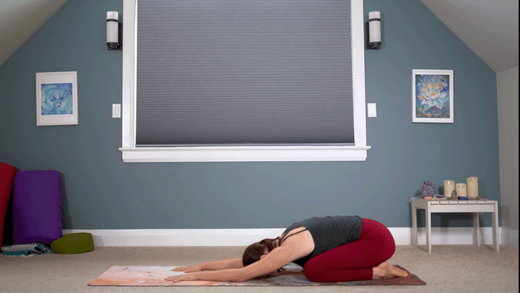 Yoga With Kassandra in Child's Pose with her hips resting on her heels and her arms extended forward