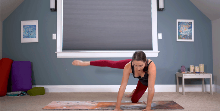 Woman on hands and knees reaching her leg out to the side on a yoga mat