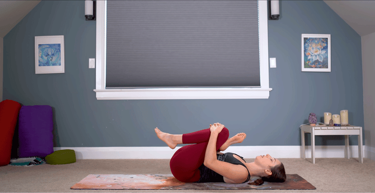 Woman lying on her back practicing a figure-4 stretch with her right ankle to her left knee