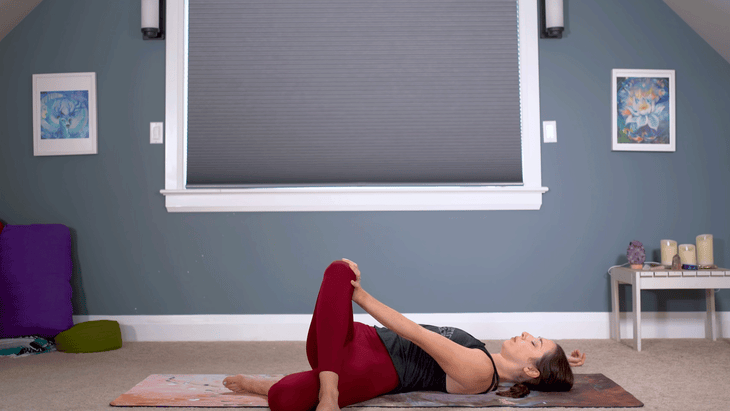 Woman on her back stretching her IT band with a figure-4 shape falling over to one side