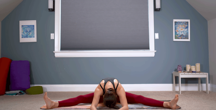 Woman sitting wide-legged on a yoga mat while sitting and stretching. 