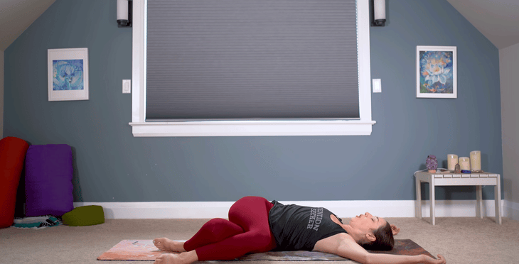 Woman lying on a yoga mat with her knees bent and over to the side to create a twist