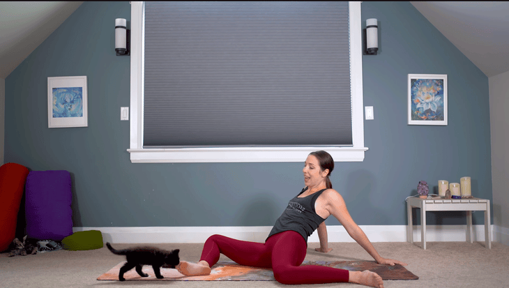 Yoga With Kassandra practicing Deer Pose, also known as 90/90, on a yoga mat with her knees bent while she leans back.