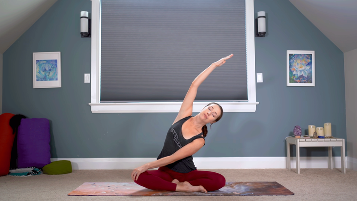 Yoga With Kassandra sitting and doing a side stretch during a feel good flow