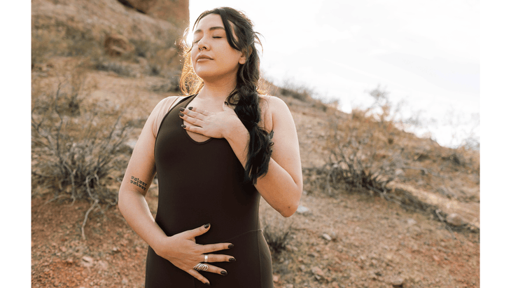 Woman standing with one hand on her chest and her other hand on her belly breathing deeply before practicing hiking stretches