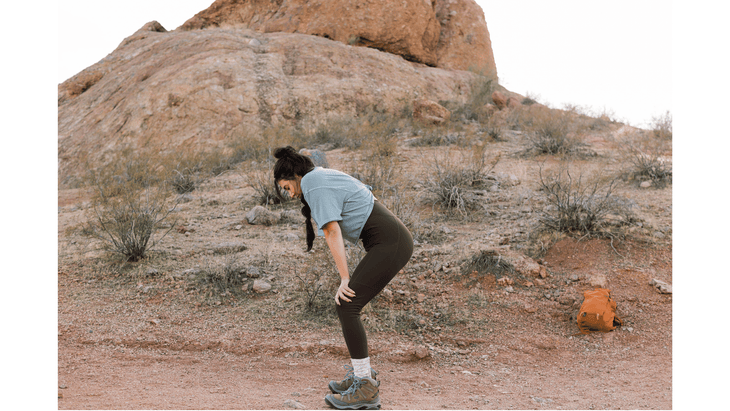 Woman hiking standing in a hiking stretch by bending her knees and rounding her back