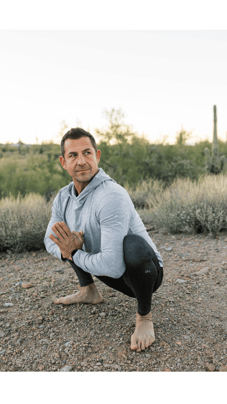 Man practicing hiking stretches, including a squat, while on the trail.