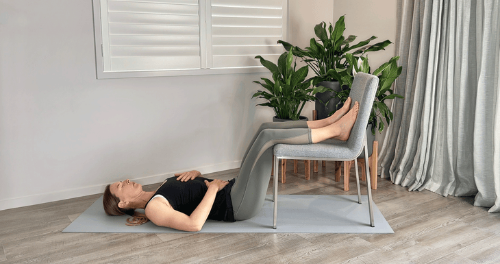 Woman lying on a mat with her calves resting on a chair