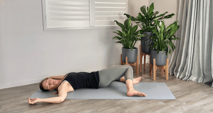 Woman lying on a yoga mat practicing psoas muscle stretches by doing reclined windshield wipers