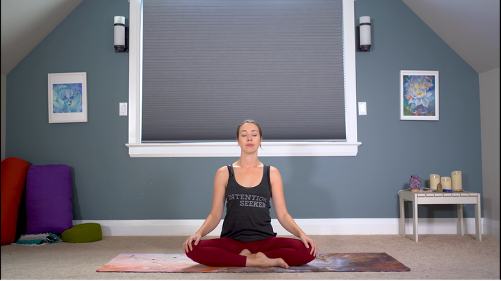 Yoga With Kassandra sitting cross-legged at the beginning of her feel good flow