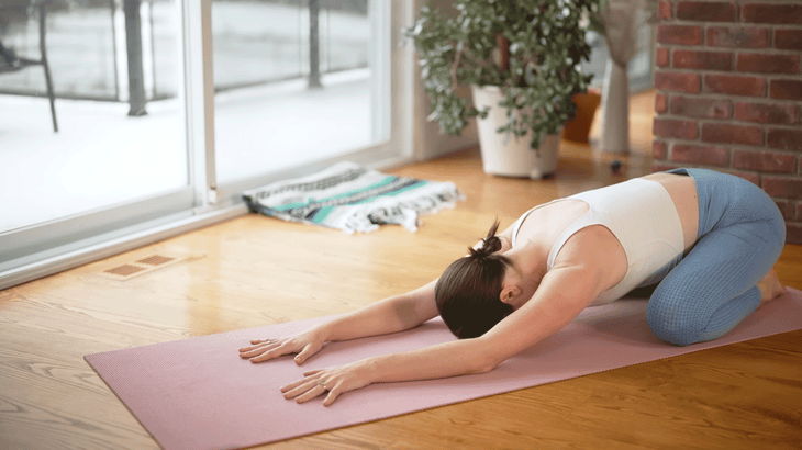 Woman on a yoga mat in Child's Pose with her arms extended, her chest low to the ground, and her hips sinking toward her heels.