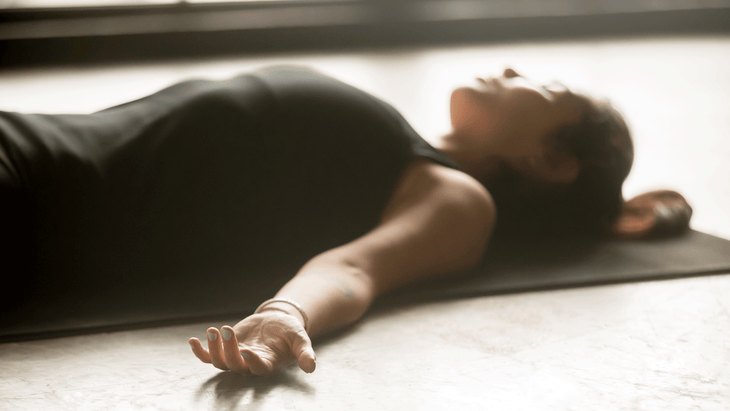 Woman lying on a yoga mat in Savasana while practicing yoga for breakups