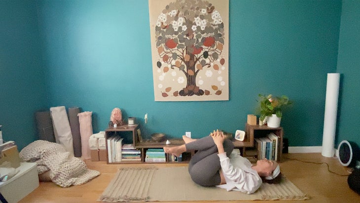 woman with legs tucked in practicing a yoga pose on a mat