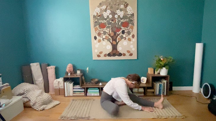 woman bending towards her left foot and practicing a yoga pose on a mat