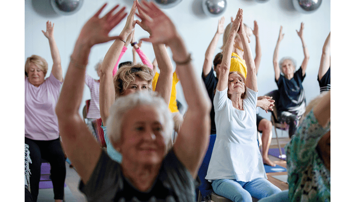 Seniors sitting in chairs and practicing yoga with their arms reaching toward the ceiling at Blue Yoga Nyla