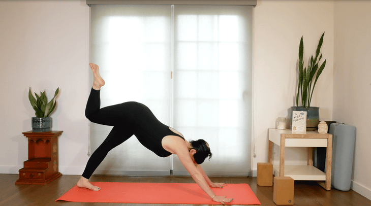 Woman practicing yoga on a mat in Downward-Facing Dog with one leg lifted