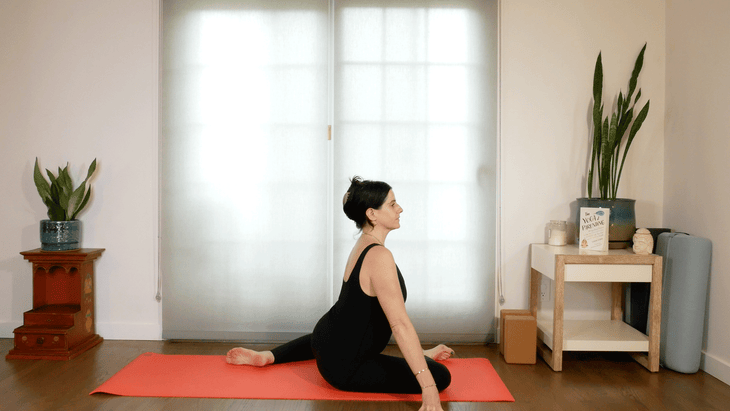 Woman on a yoga mat practicing deer pose, also known as 90/90