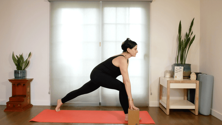 Woman practicing a lunge on a yoga mat with blocks beneath her hands
