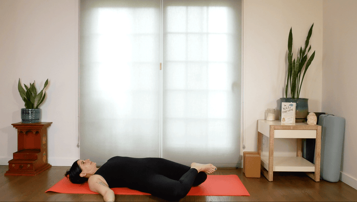 Woman lying on her back on a yoga mat practicing windshield wipers