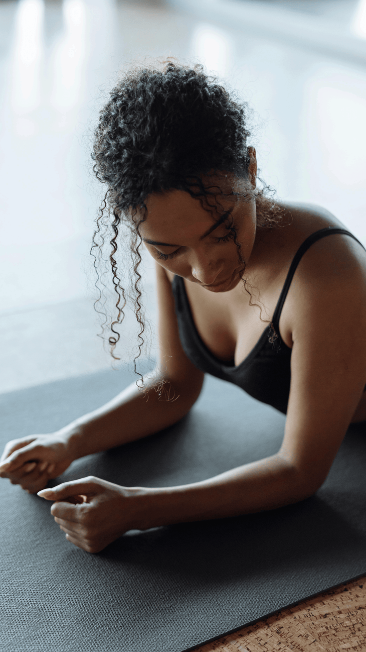 Woman in Sphinx Pose on a yoga mat with her forearms on the mat and her chest lifted as she looks contemplative