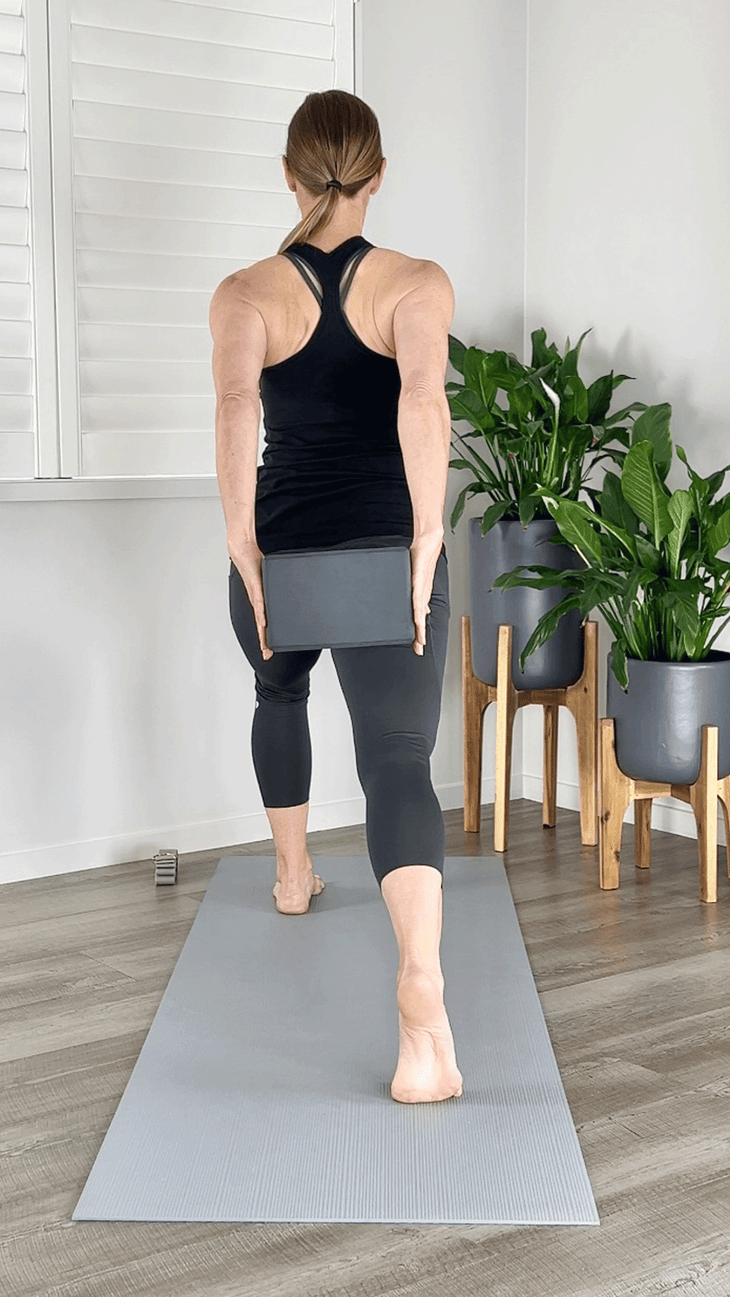 Woman in a lunge on a yoga mat squeezing a block between her hands