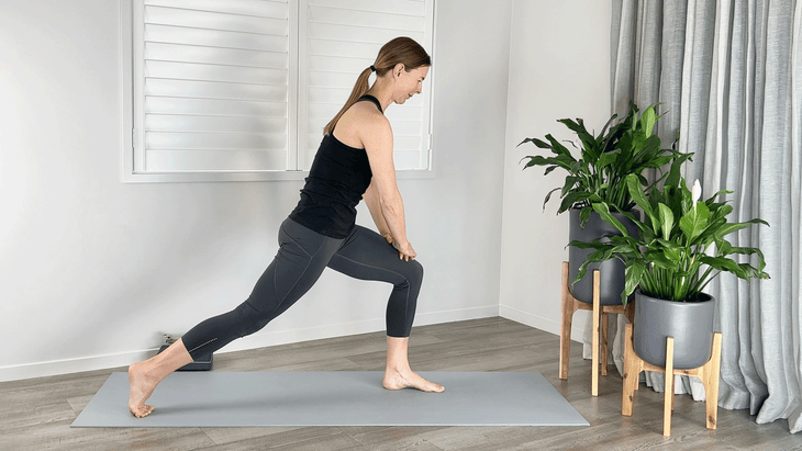 Woman practicing a High Lunge variation on a yoga mat with the hands on the thigh and a rounding of the back