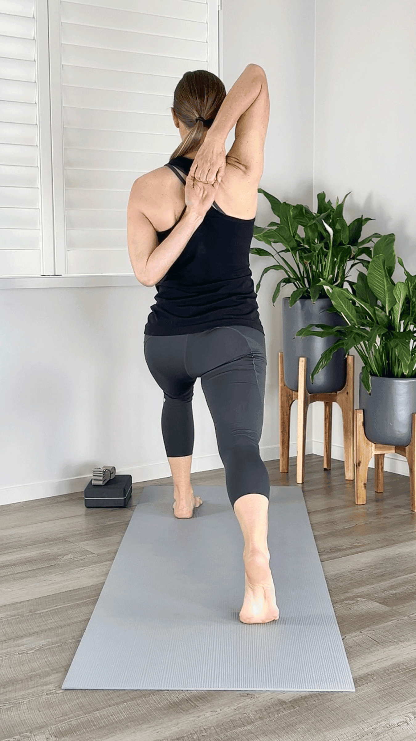 Woman standing on a yoga mat in a lunge with her arms in Cow Face positionclasping her fingertips behind her back