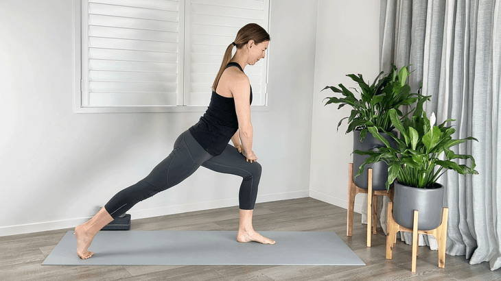 Woman on a yoga mat with her hands on her thighs in a lunge arching her back