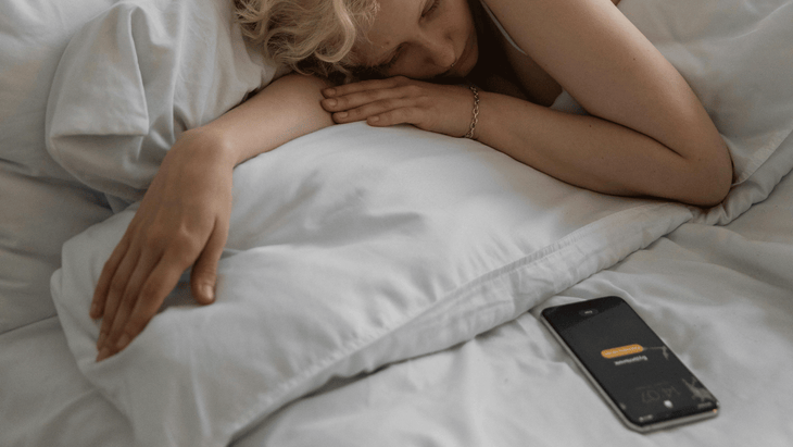 Woman lying in bed with her phone alarm on snooze as she readies herself to practice a 20-minute morning yoga