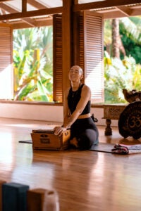 Image of yoga teacher Kirin Power playing an instrument in a yoga studio with windows behind her.