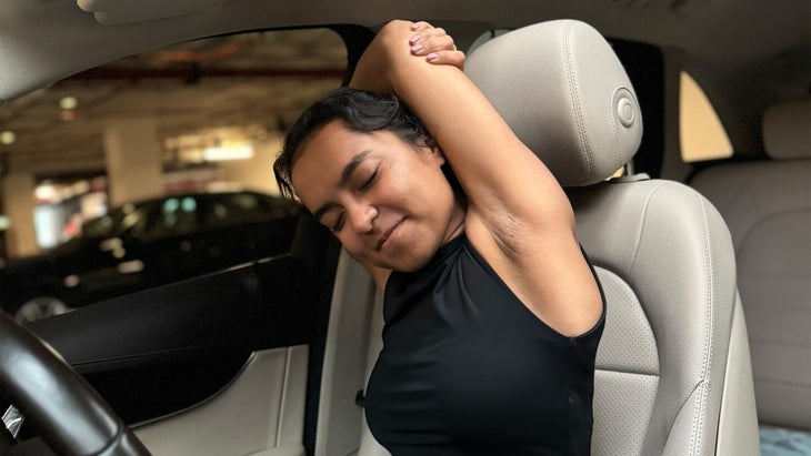 woman practicing yoga in her car with her arms crossed over her head leaning to the side