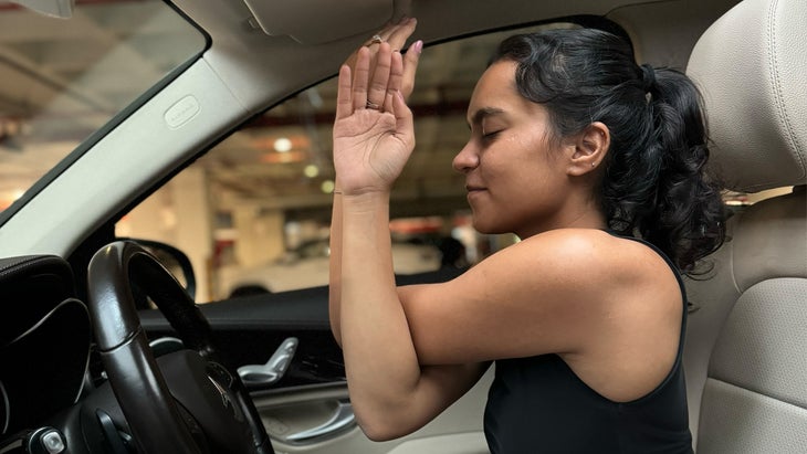 woman practicing yoga in her car with crossed arms and palms touching