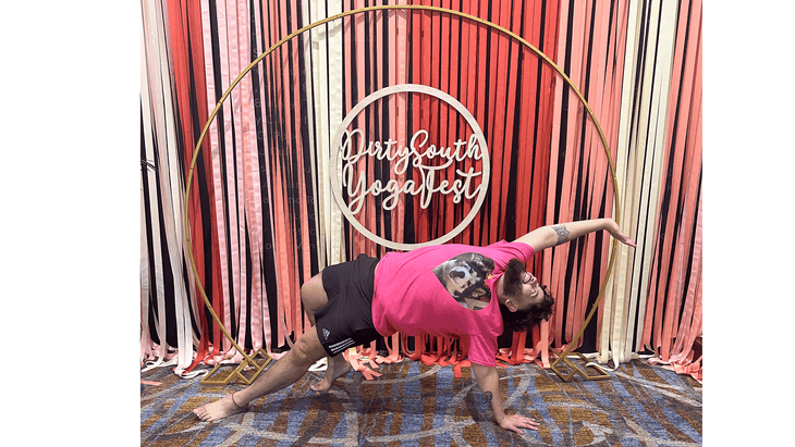 A photo of a guy practicing Wild Thing in front of the Dirty South Yoga Fest logo