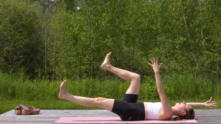 woman practicing yoga on mat outdoors in dead bug pose