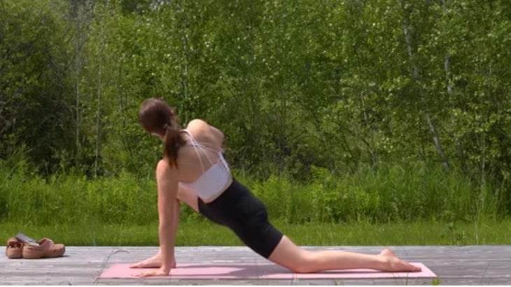 woman practicing yoga on mat outdoors in twisted lunge