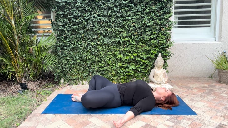 woman practicing yoga outdoors on a mat laying on her back in butterfly pose